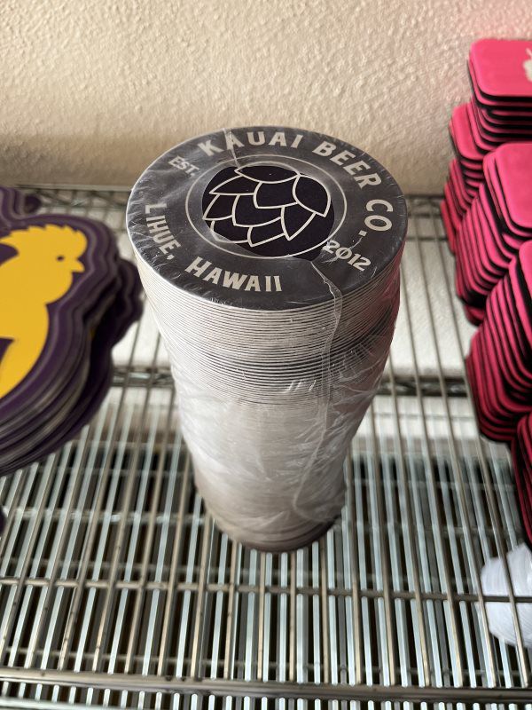 Shrink-wrapped sleeve of black Kauai Beer Co. coasters with a hop-cone logo