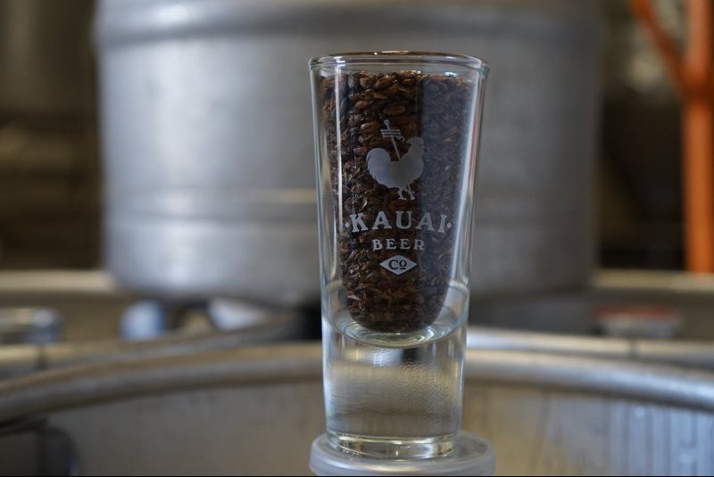 Etched Kauai Beer Co. taster glass in front of a brewery tank